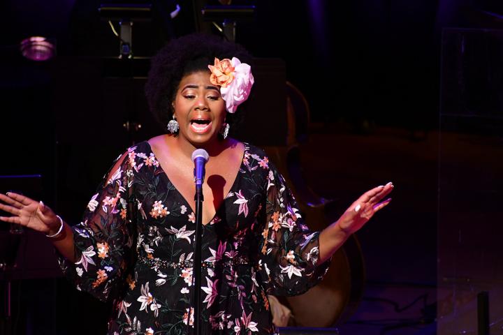 Black woman in a flowery dress singing into a microphone.