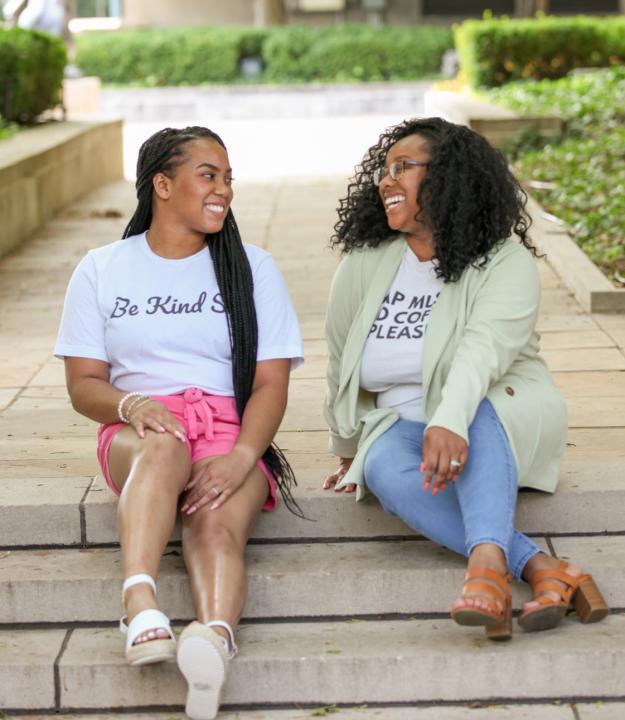 Two black women sitting on stairs talking.