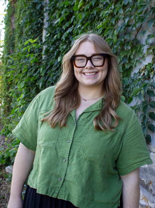 Addie Linn standing in front of ivy wall.