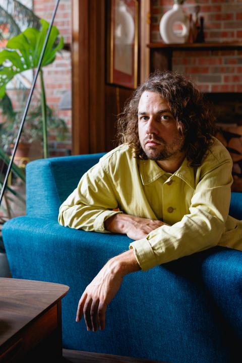 Kevin Morby leaning over the arm of a blue chair