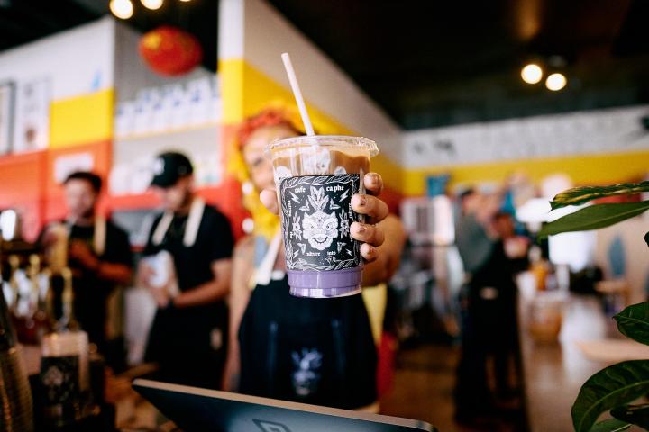 Employee holding a purple specialty drink at Café Cà Phê