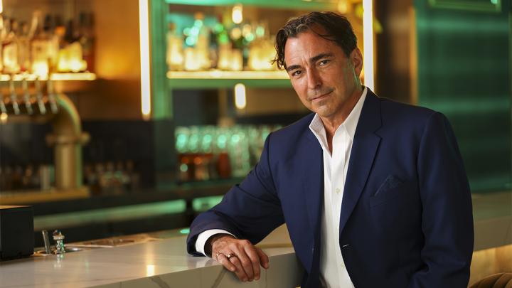 David Manica in a suit sitting at a bar.