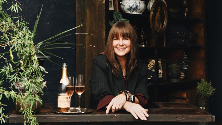 Heather White standing at a counter and smiling, next to a bottle of champagne and two glasses.