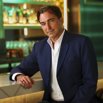 David Manica in a suit sitting at a bar.