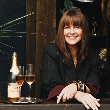 Heather White standing at a counter and smiling, next to a bottle of champagne and two glasses.